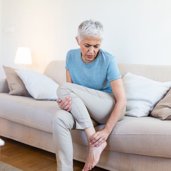 Old age, health problem and people concept - senior woman suffering from pain in leg at home. Senior woman holding her foot with pain.